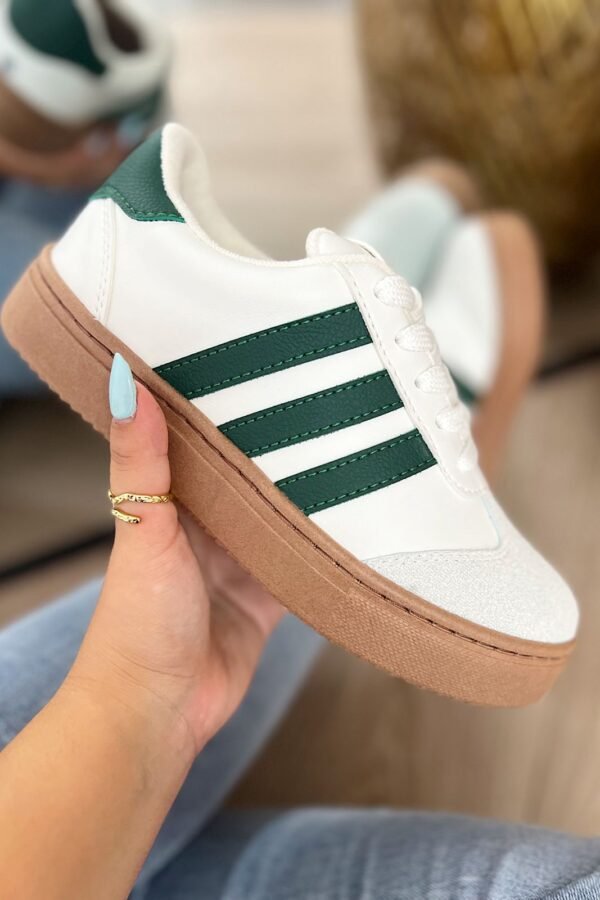 Tenis Addi blancos con detalles verdes, suela color café y tres líneas laterales verdes. Diseño cómodo, versátil y moderno para uso diario.