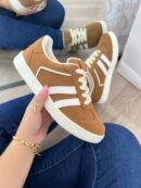 Tenis Addi miel con detalles verdes, suela color café y tres líneas laterales verdes. Diseño cómodo, versátil y moderno para uso diario.